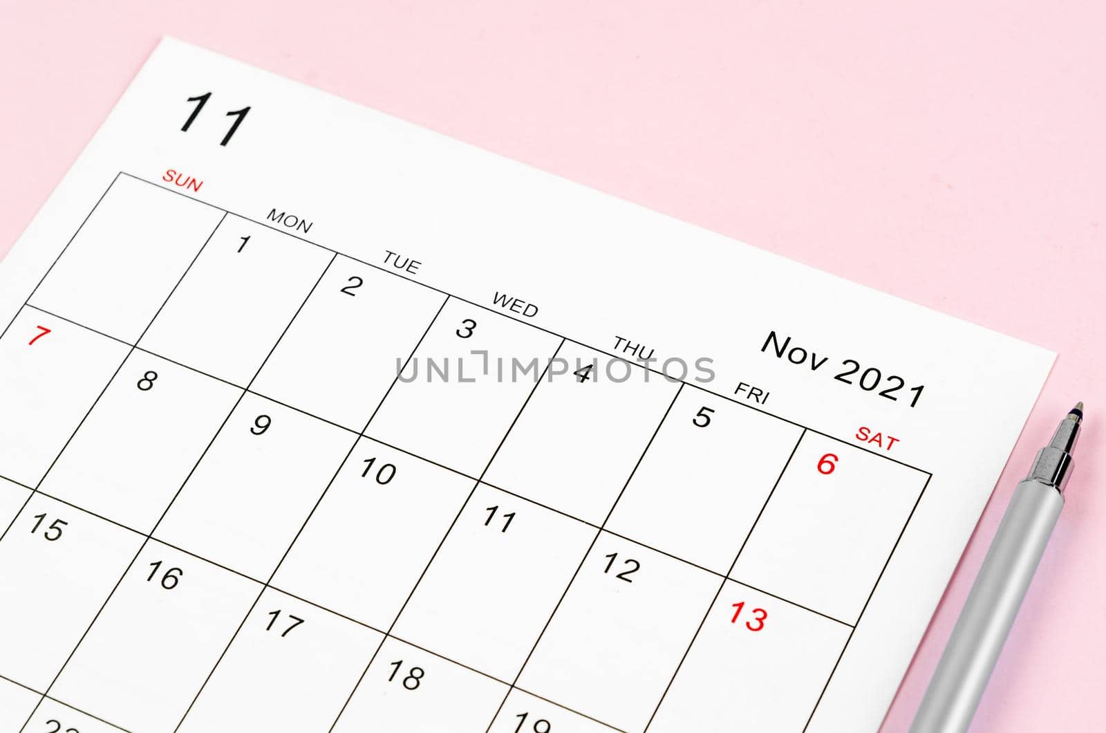 Close up November 2021 calendar sheet with pen on pink background.