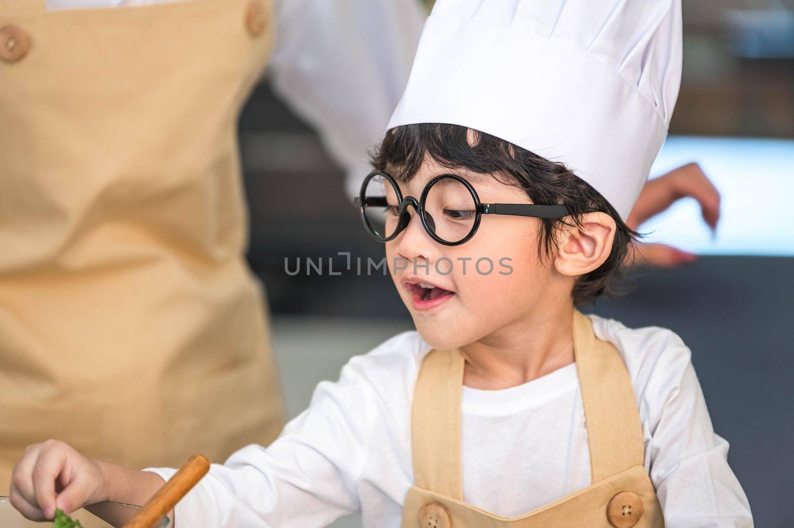 Closeup of Asian cute little boy wearing chef hat and apron with mother in home kitchen. Thai people and lifestyles concept. Job occupation and Education learning concept. Happy family time theme