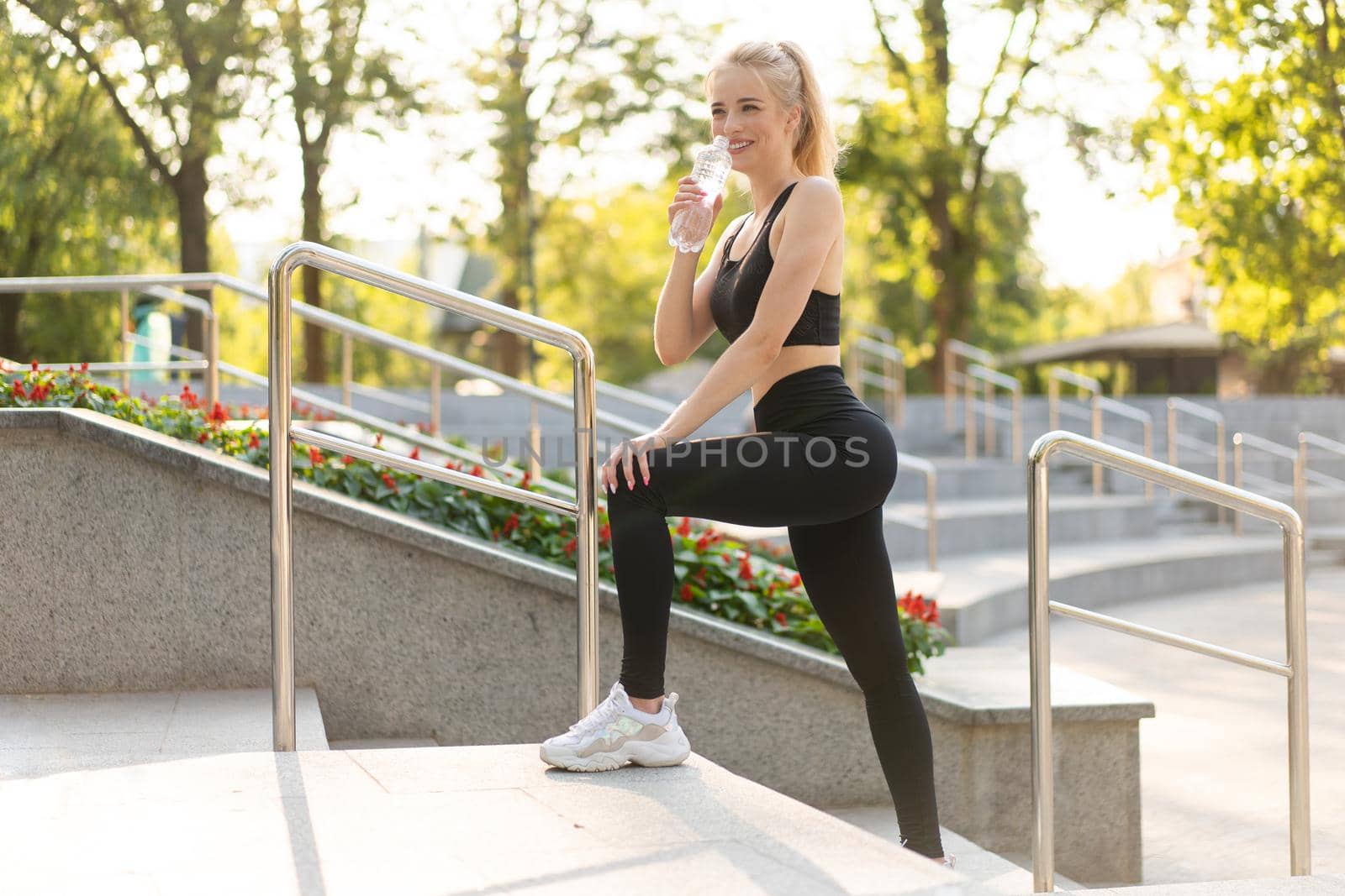 Sport and Fitness. Young Caucasian Woman Dressed Sportswear Standing Outdoor Drink Water Plastic Bottle Summer Park Sunlight Background Resting After Training Jogging Running Exercises