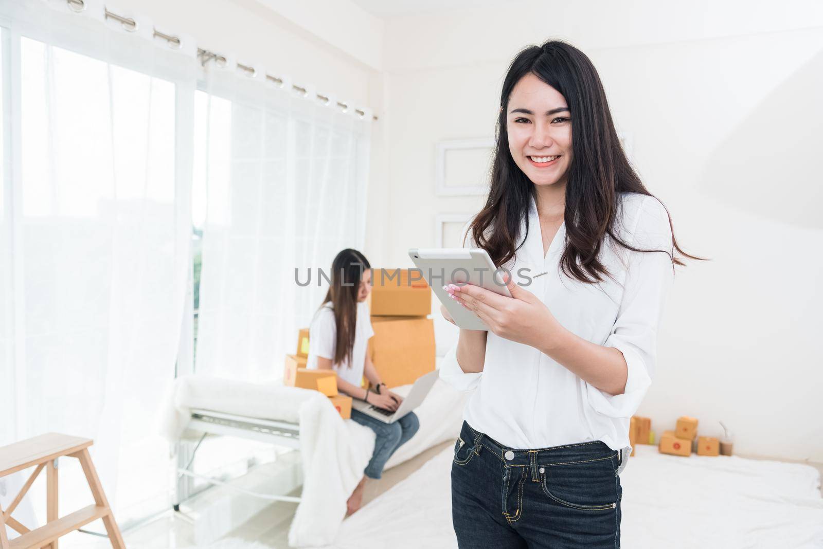 Beauty Asian woman using tablet for checking order from customers at home. Business and Delivery transportation concept. Logistic service and Product packing theme. Girl looking at camera