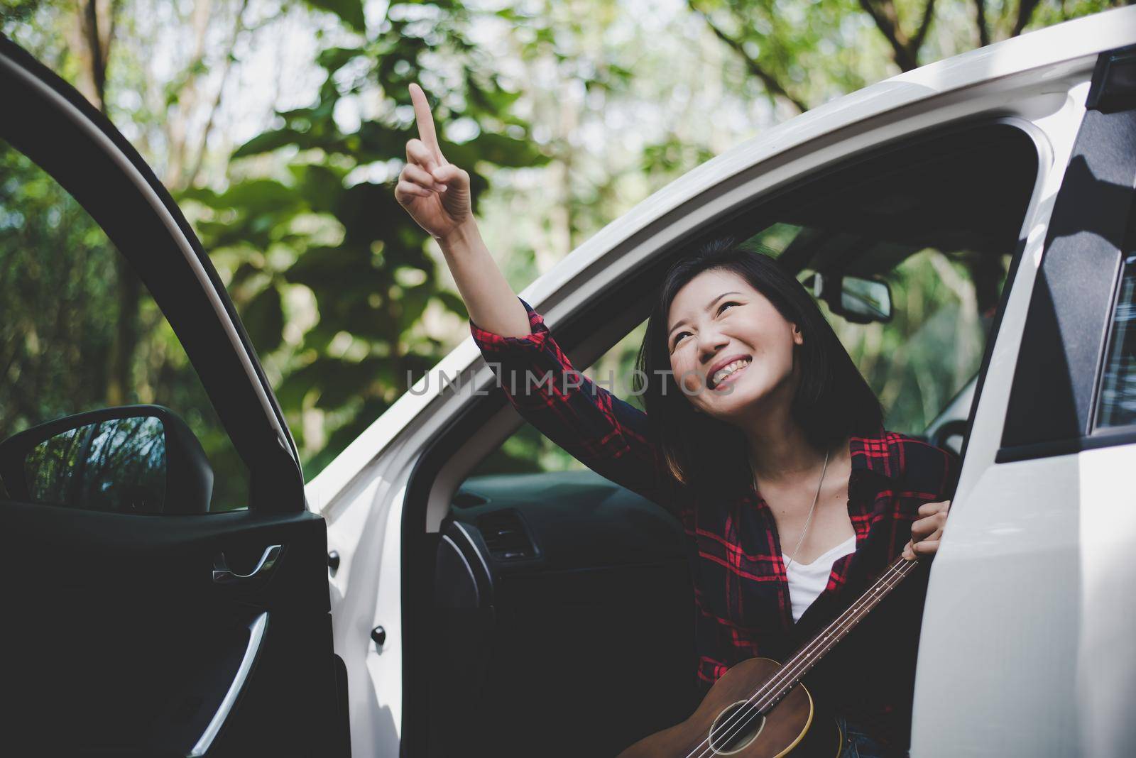 Beauty Asian woman pointing and having fun at outdoors summer with Ukulele in white car. Traveling of photographer concept. Hipster style and Solo woman theme. Lifestyle and Happiness life theme. by MiniStocker