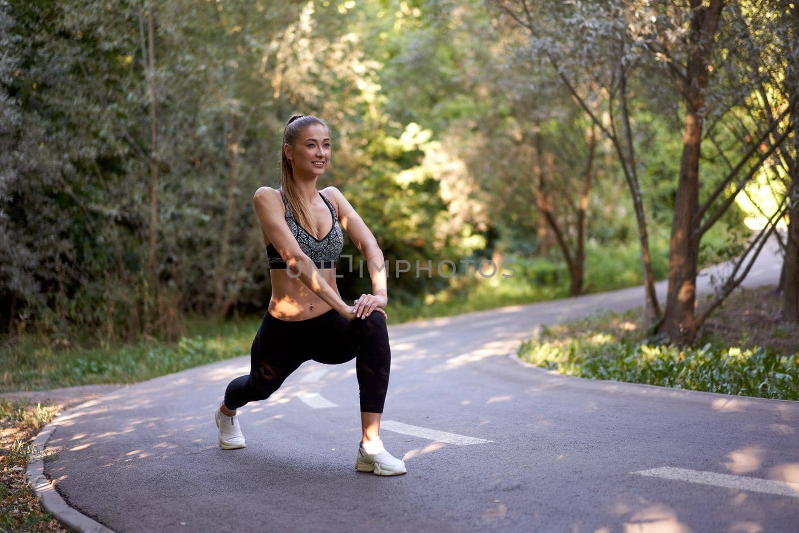 Woman runner stretching legs before exercising summer park morning Middle age athletic female warming up body before running Caucasian person warm up jogging running track