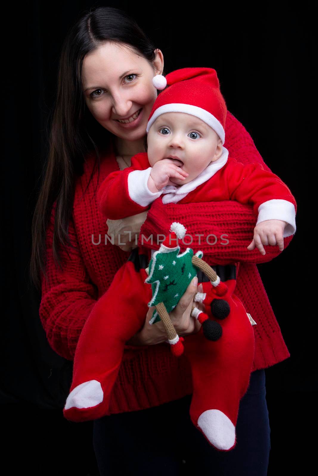 Mom and little child at Christmas. A woman holds her son in her arms, who is dressed in Santa Claus clothes.