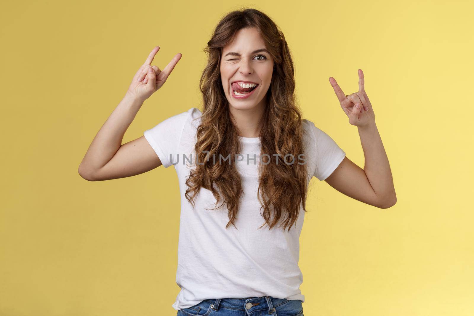 Awesome party having fun. Daring attractive carefree girl enjoy excellent event show rock-n-roll heavy metal gesture mimicking funny expressions wink stick tongue stand yellow background amused by Benzoix