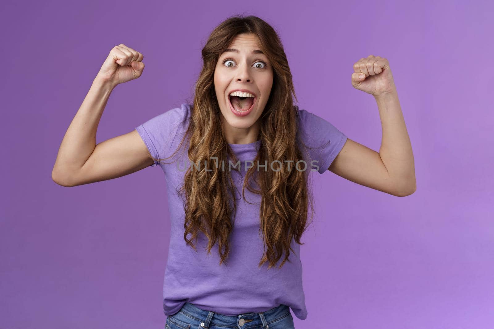 Excited happy cheerful curly-haired girlfriend cheering encourage team win rooting for friend raise hands fist pump celebration yelling enthusiastic, triumphing celebrate victory achievement.