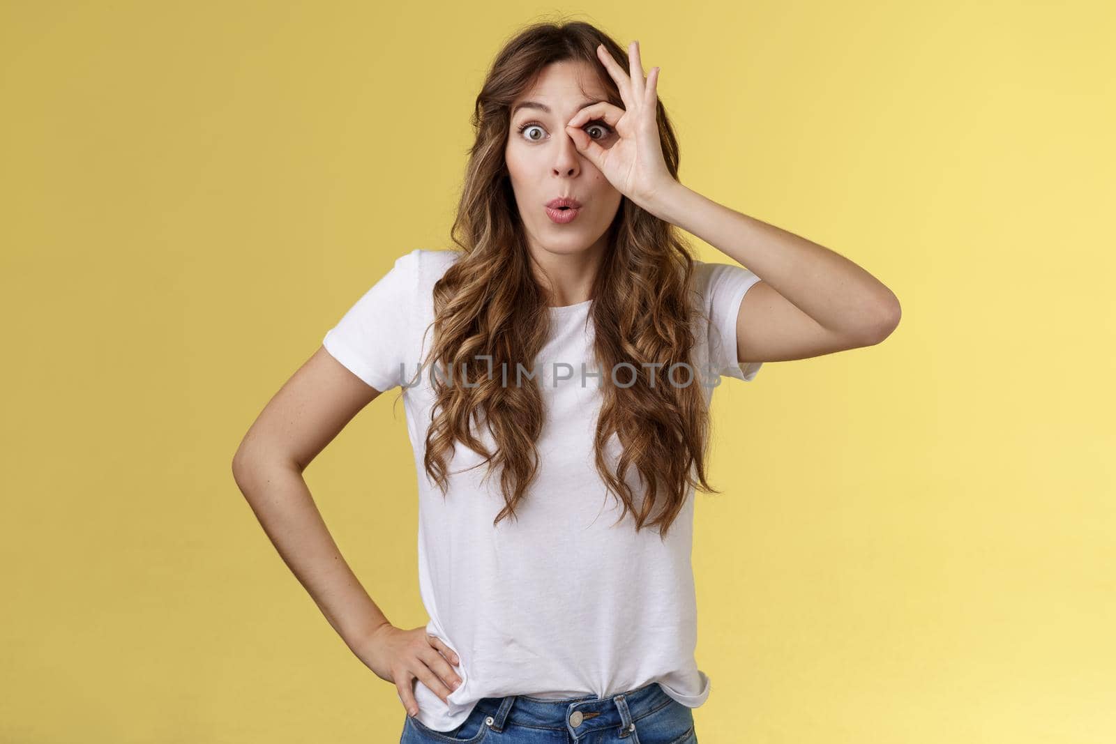 Attractive young astonished curly-haired european girl fascinated folding lips admiration stare alluring thing spot awesome promo hold ring gesture okay ok through eye check out interesting spot. Lifestyle.