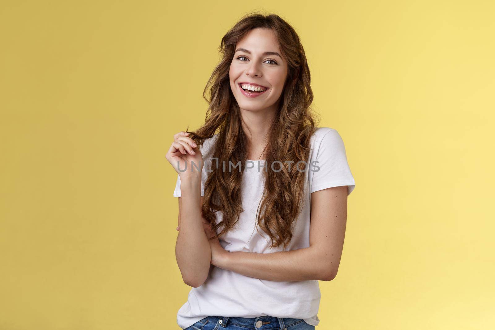 Lively joyful happy cute brunette curly long hairstyle playing curl laughing joyfully having funny amusing conversation smiling toothy white perfect smile stand yellow background relaxed by Benzoix