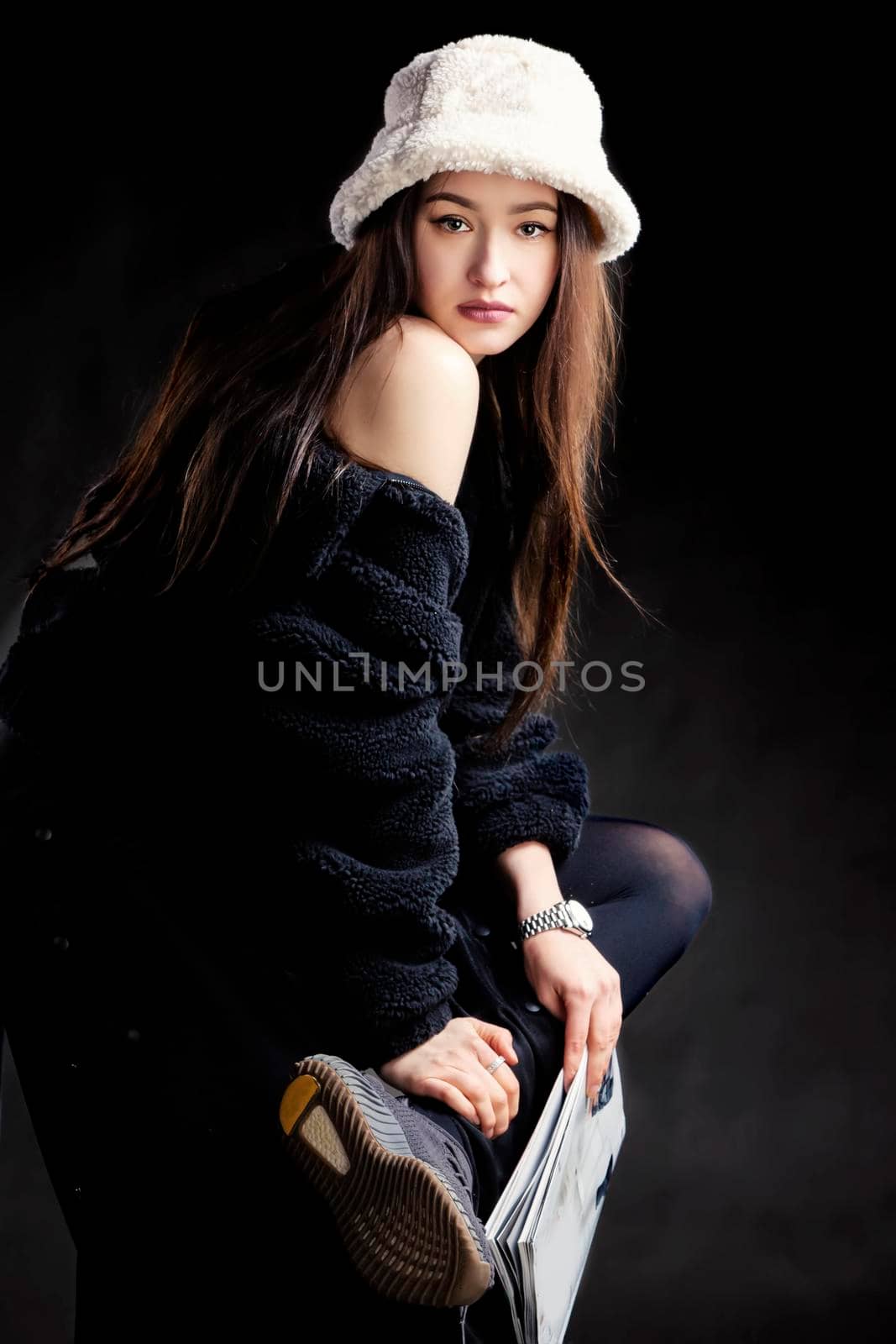 Beautiful stylish girl in dark clothes and a fashionable hat against a dark background.