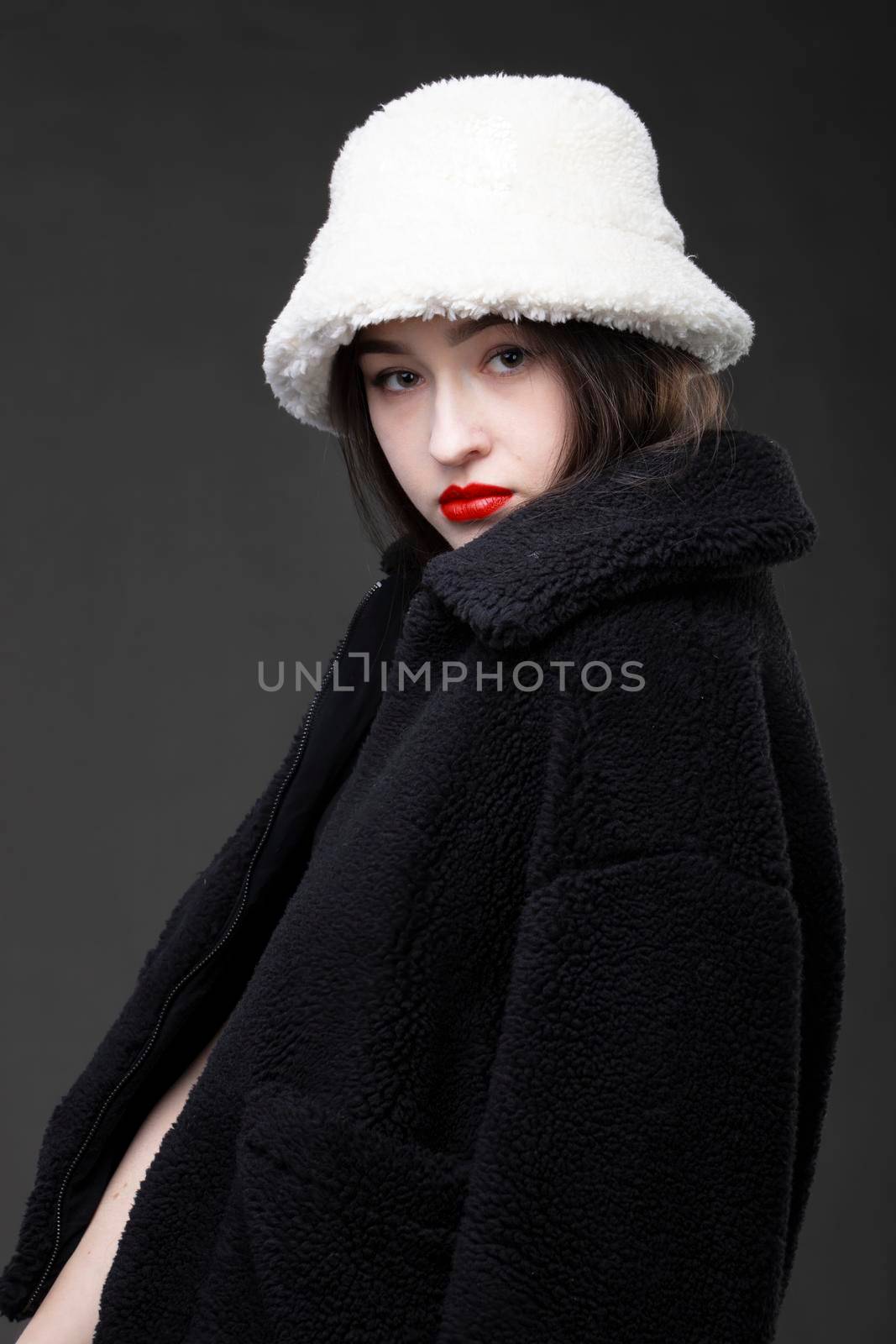 A beautiful girl in a white fur hat and a black fur coat on a gray background.