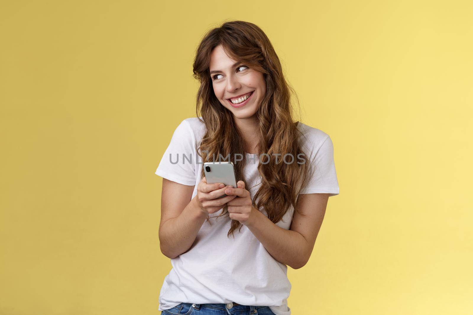 Lovely silly cute flirty girl texting receive romantic lovely gesture look away blushing modest smiling broadly reading bold passionate message stand yellow background joyfully send boyfriend photo. Lifestyle.