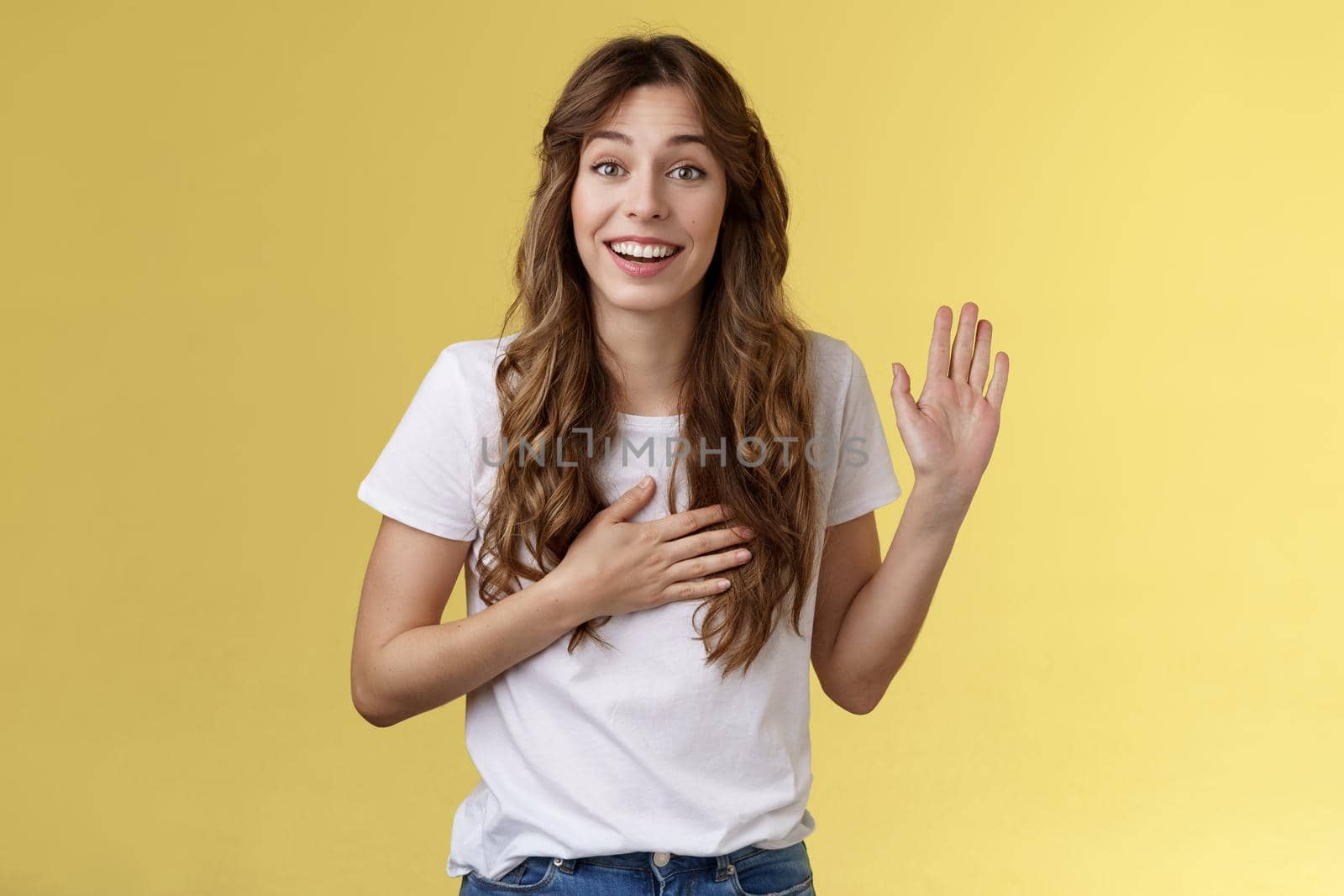 Girl introduce herself friendly joyful casual conversation smiling broadly hold hand heart raise palm waving swear tell truth be honest grinning make promise oath stand yellow background say hi. Lifestyle.