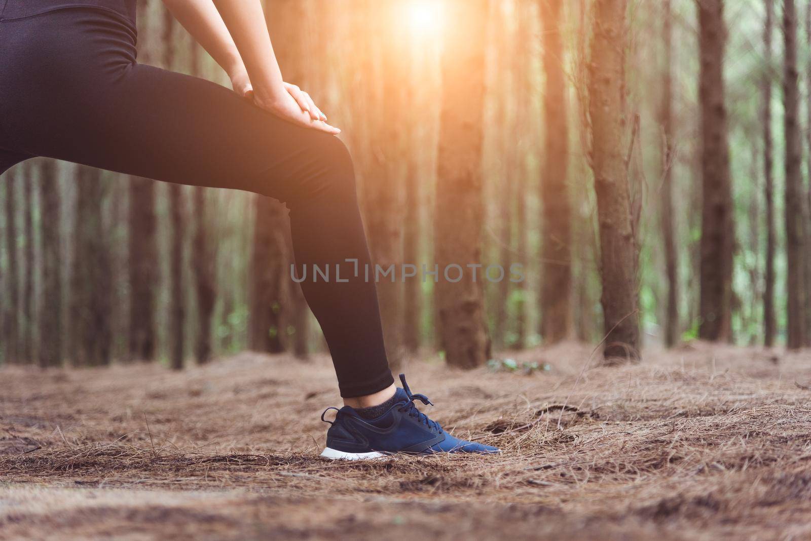 Close up of lower body of woman doing yoga and stretching legs before running in forest at outdoors. Sports and Nature concept. Lifestyle and Activity concept. Pine woods theme.