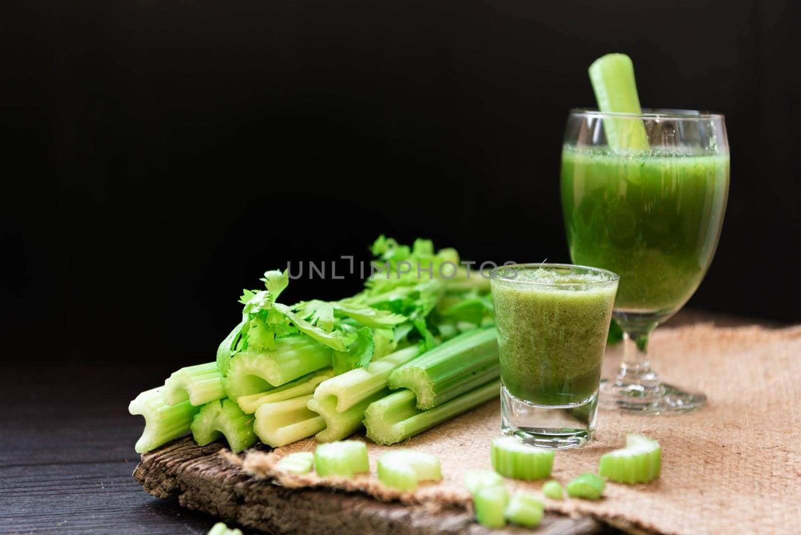 Blended Celery juice in welcome drink glass and bunch of fresh celery stalk on wooden table with leaves on black background. Food and ingredients  of healthy vegetable. Freshness herbal for dieting