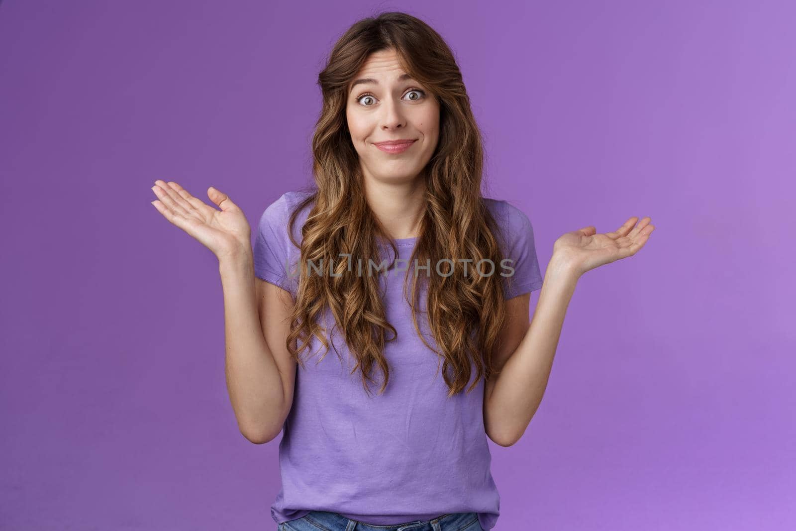 Girl not giving any care. Carefree unbothered cute caucasian curly-haired woman shrugging hands spread sideways smirking uninterseted nothing to say shake head questioned clueless purple background.