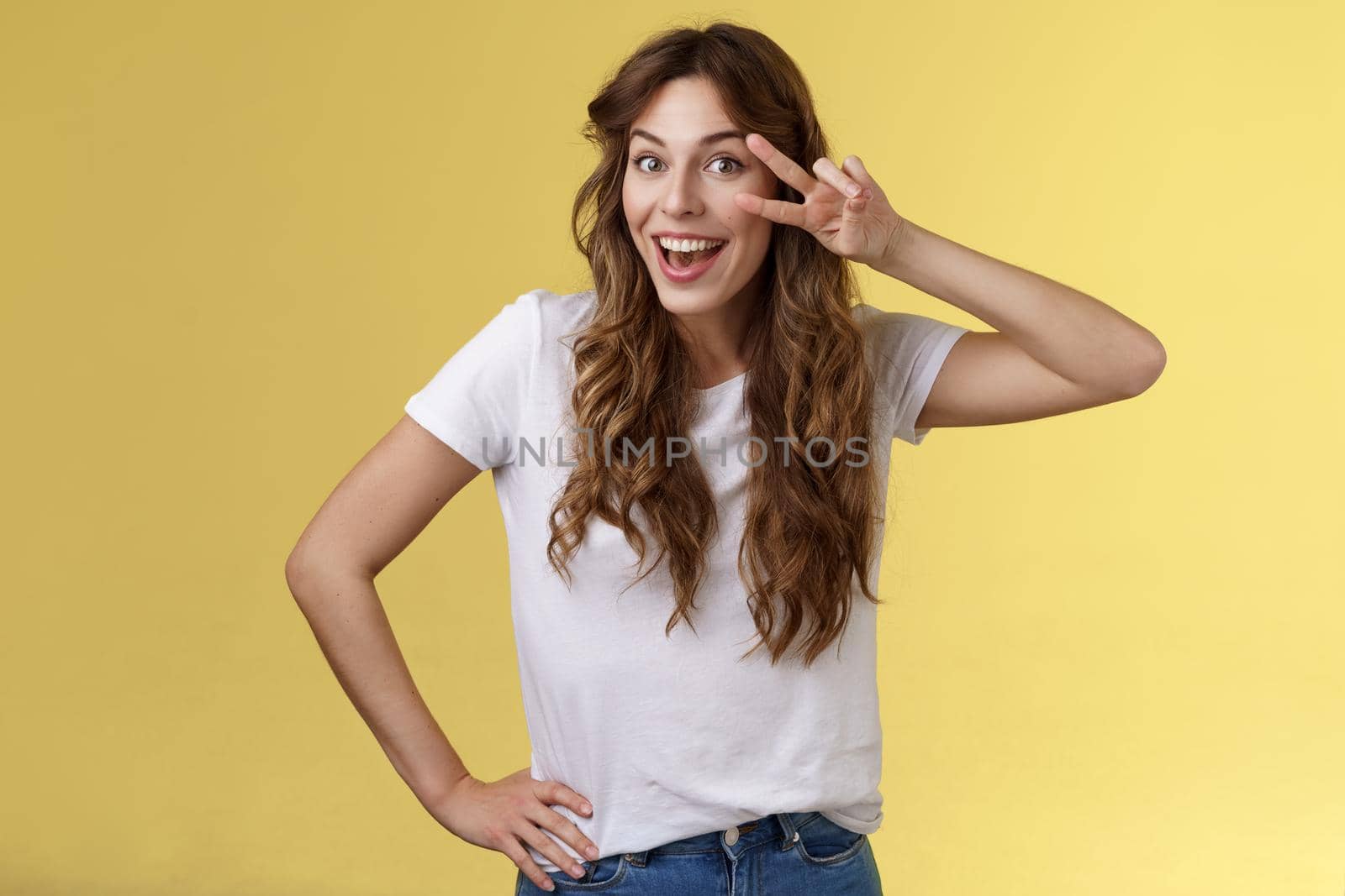 Playful surprised charismatic young caucasian girlfriend having fun look amused enthusiastic show peace victory sign laughing smiling joyfully enjoy summer holidays touch hip stand yellow background by Benzoix