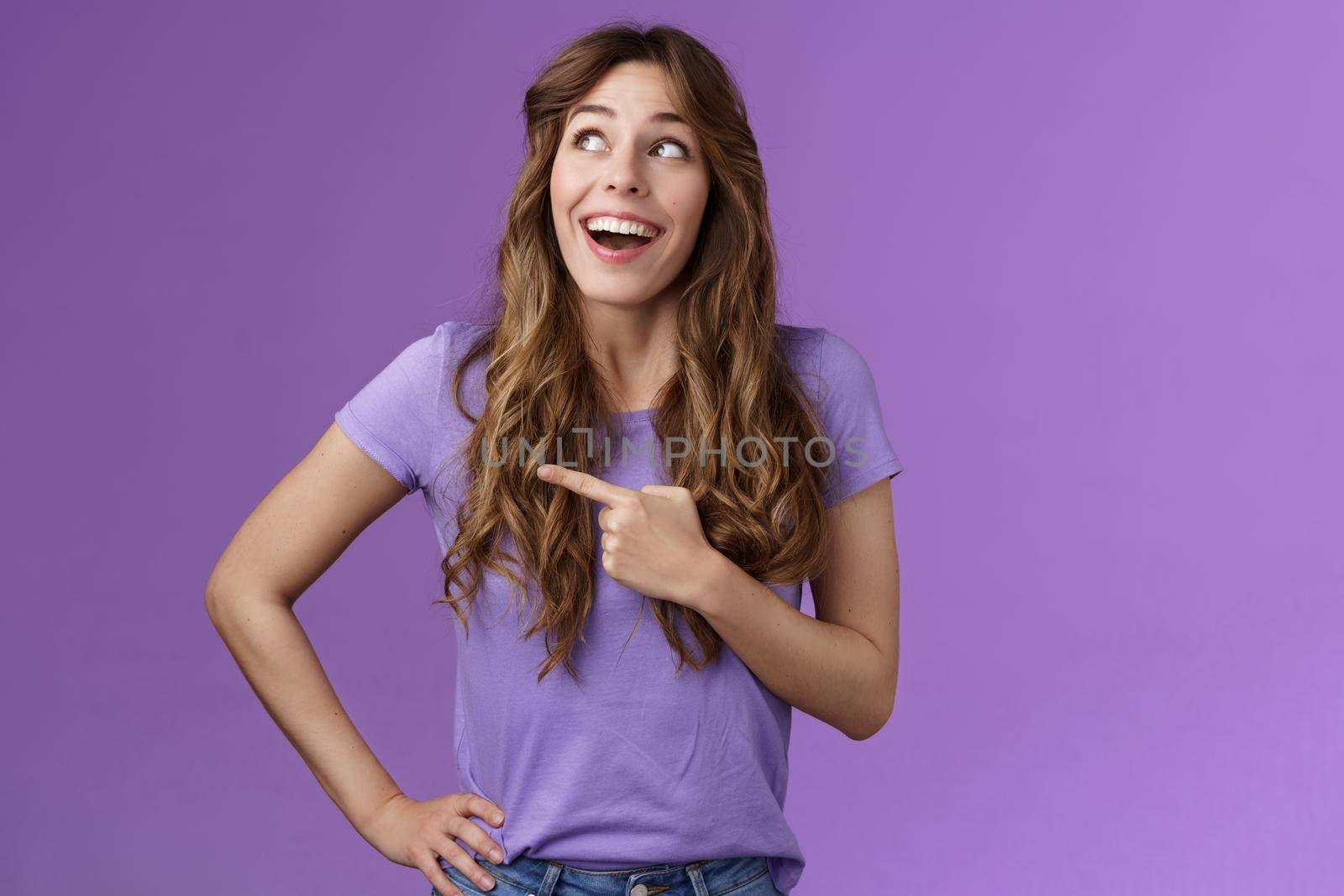 Dreamy wondered impressed cute lively excited positive girl feel happy travel abroad explore new city tourist trip smiling broadly contemplate awesome view look pointing left grinning purple wall. Lifestyle.