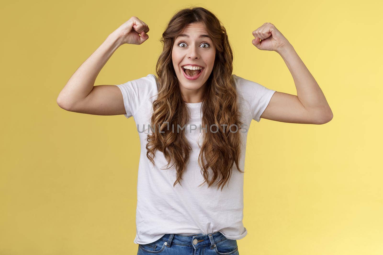 Lucky girl feeling like winner. Triumphing excited cheerful young woman raise hands fist pump up celebratory smiling broadly thrilled yelling supportive root favorite team reach success by Benzoix