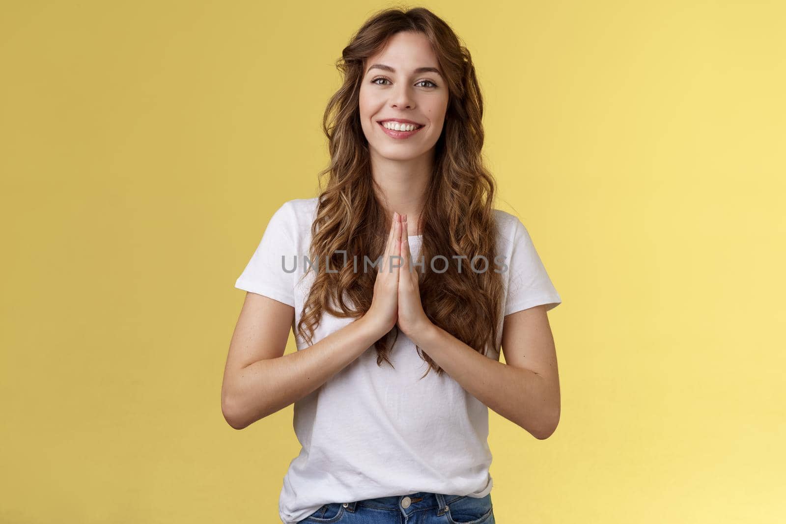 Cheerful confident outgoing young polite girl say namaste greeting asian guests smiling gladly thanking for visit hold hands pray supplication gesture asking favour begging stand yellow background. Lifestyle.