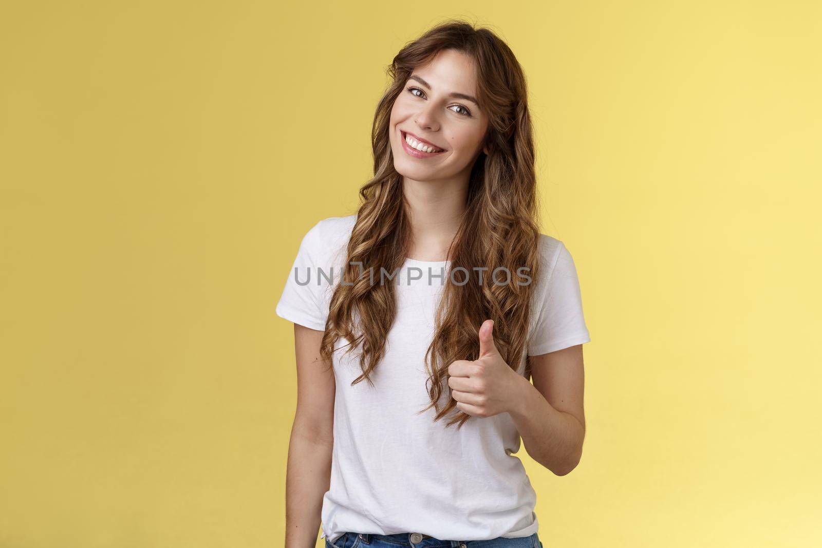 Well done congratulations. Happy charismatic pretty european female tilt head smiling broadly accept agree your idea like satisfied good result show thumb up approval gesture yellow background by Benzoix