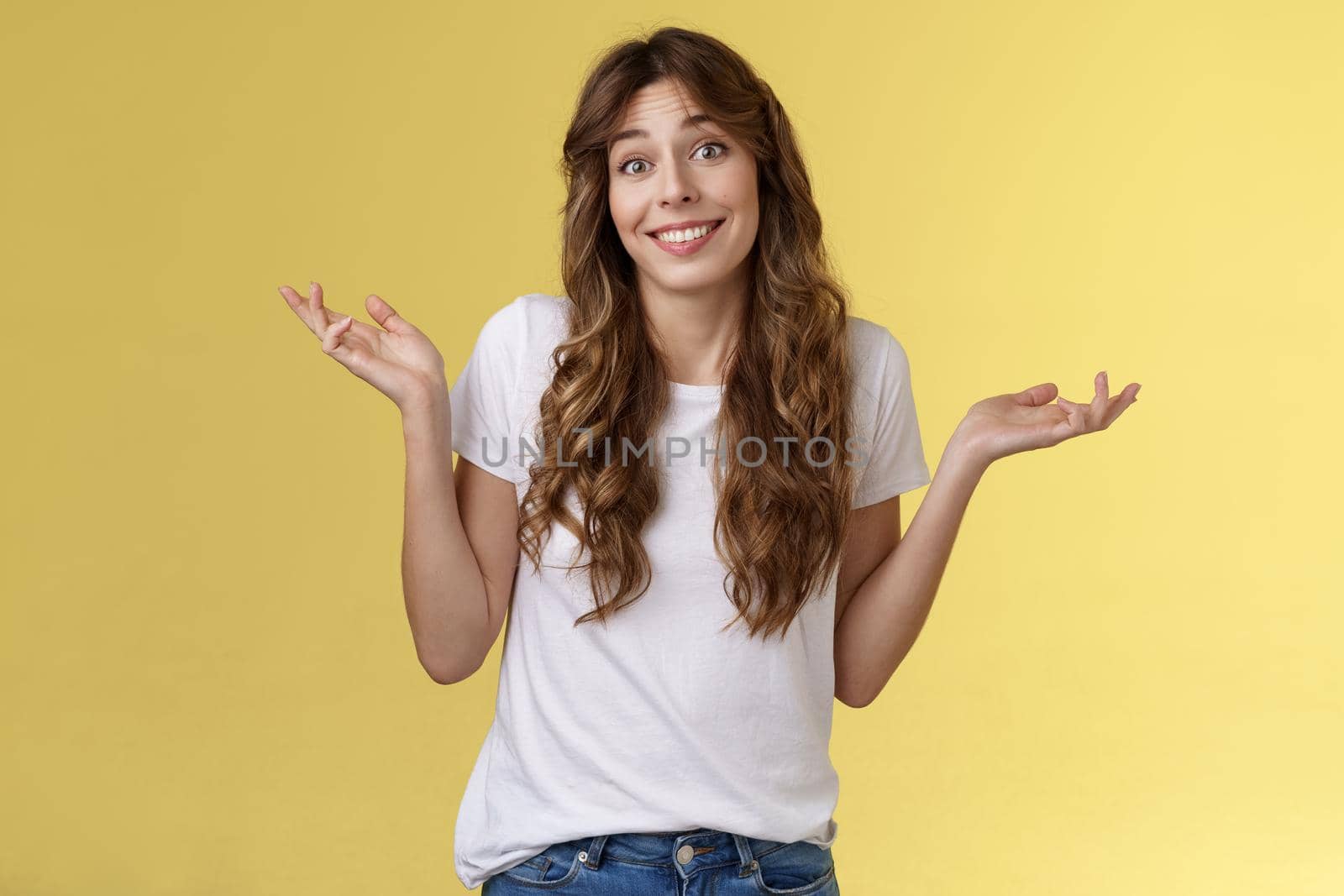 Who cares have fun. Carefree indifferent outgoing happy young woman shrugs raise hands sideways clueless unbothered apathic to topic uninterested smiling broadly careless yellow background.