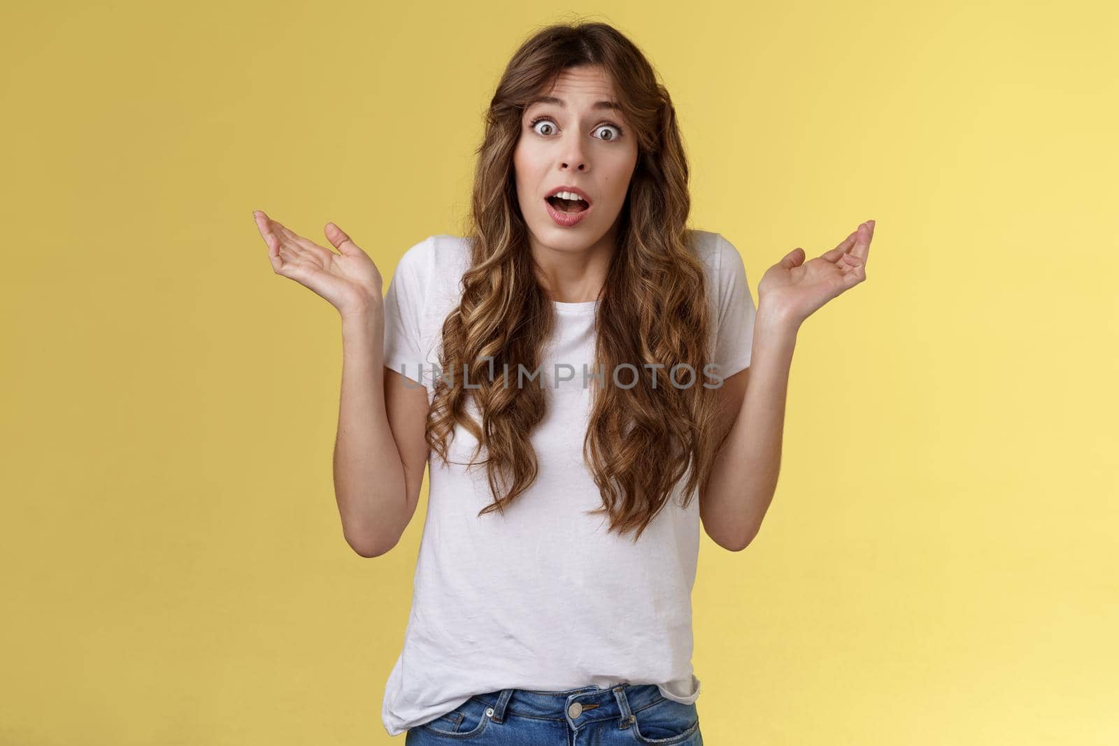 I not know. Clueless confused cute nervous young woman shrugging hands raised sideways full disbelief questioned expression lift eyebrows puzzled unable answer question stand yellow background.