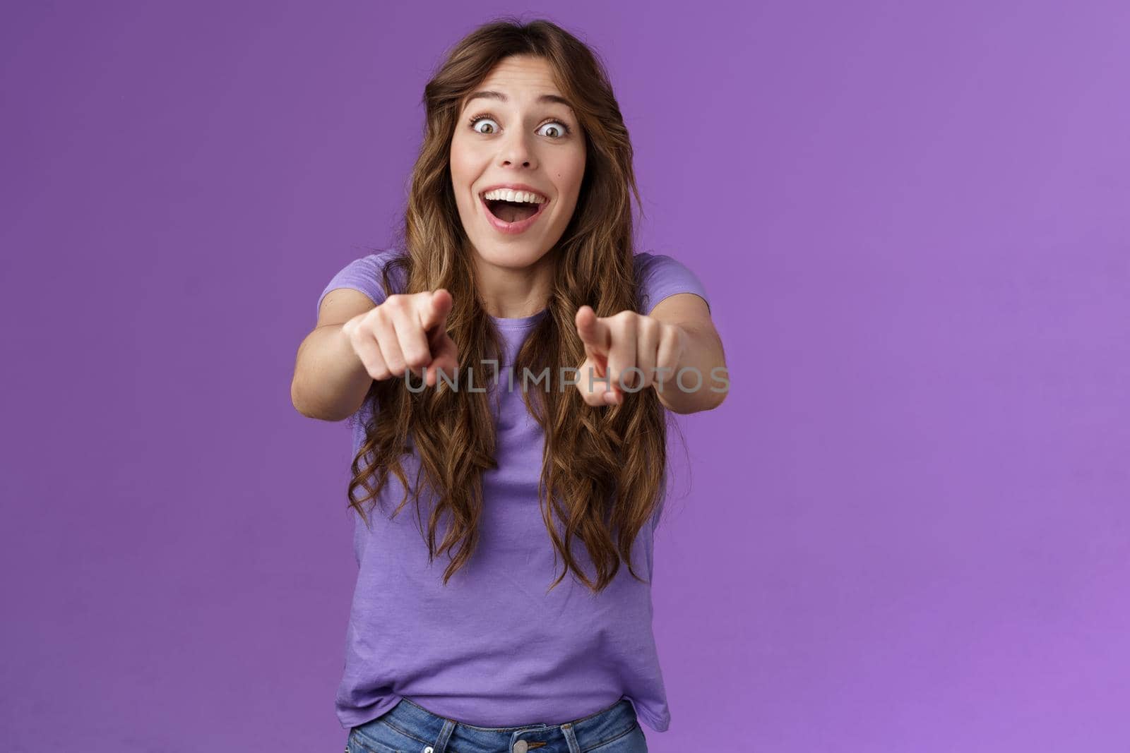 Omg its you. Surprised girl fan cheering joyfully gazing camera popping eyes pointing fingers forward astonished express admiration see superstar wanna receive autograph stand purple background by Benzoix