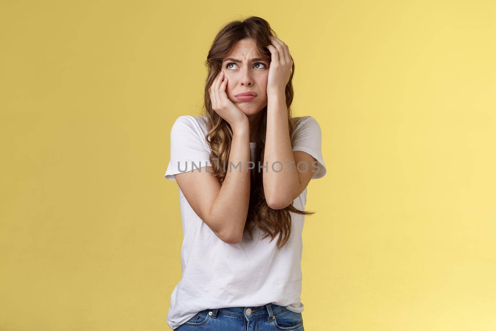 Shocked timid insecure young panicking woman wanna cry standing anxious frightened grab head both hands freak out look away praying for help terrified stand yellow background horrified. Lifestyle.