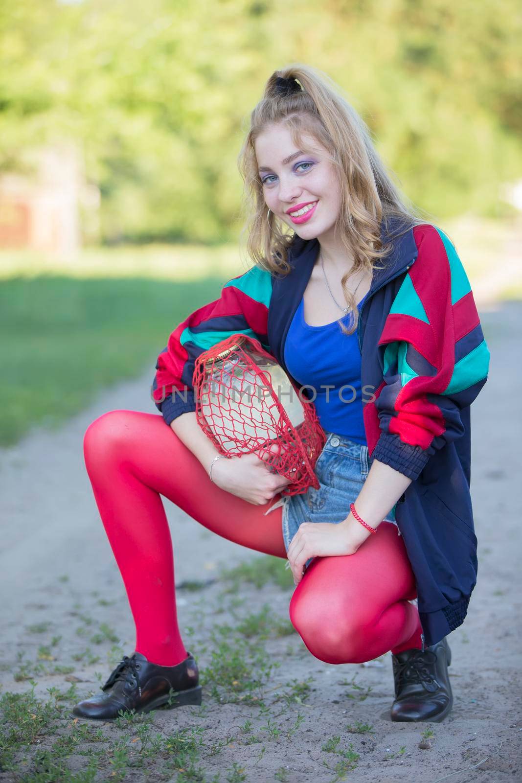 A beautiful 90s country girl in bright clothes holds a string bag with a can of birch sap. Russian Woman in the style of the 90s.