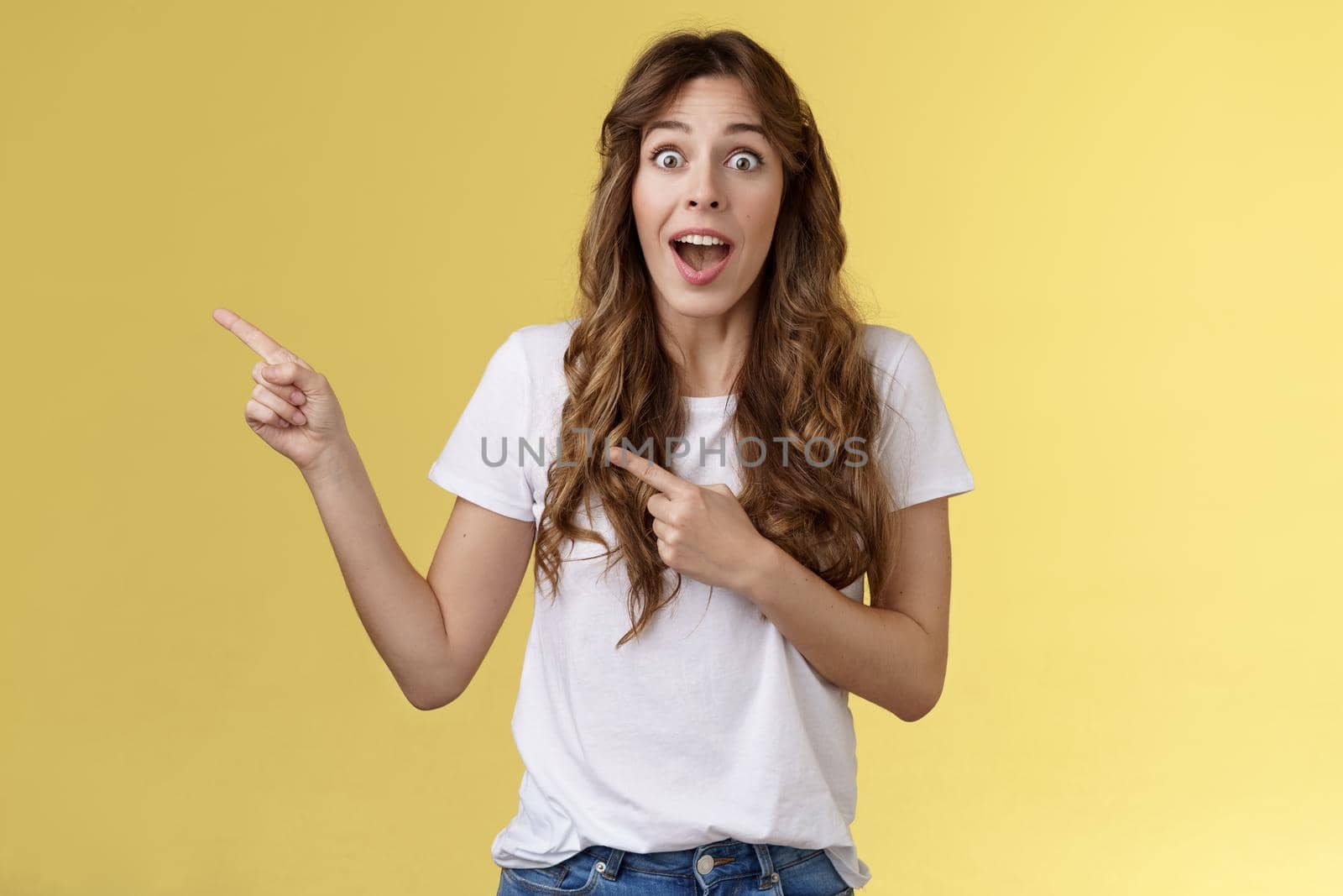 Excellent offer right behind corner. Amused surprised enthusiastic speechless cheering girlfriend scream impressed excited stare camera astonished pointing index fingers left yellow background.