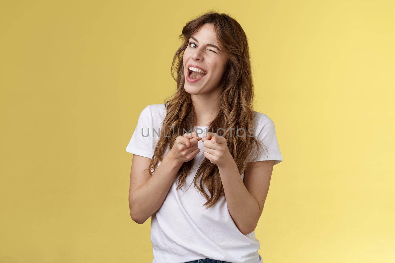 Sassy good-looking caucasian curly-haired girl hinting awesome party comming winking cunning cheeky smiling pointing index finger camera approve friends outfit congratulate good job.