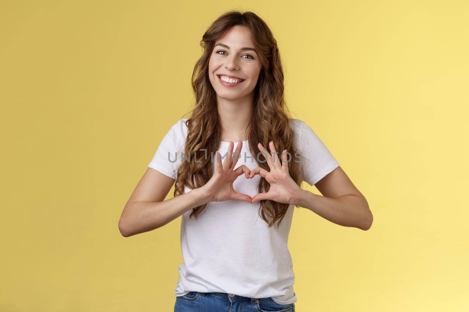 You my valantine. Tender confident adult girl curly hairstyle show heart gesture near chest express romantic sympathy feelings smiling delighted cherish relationship boyfriend yellow background by Benzoix