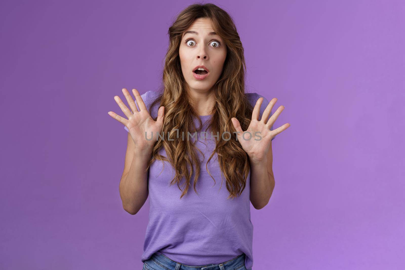 Ambushed shocked girl gasping not expect friend jump out corner raise palms surprised astonished drop jaw open mouth stunned stare camera impressed stupefied purple background. Copy space