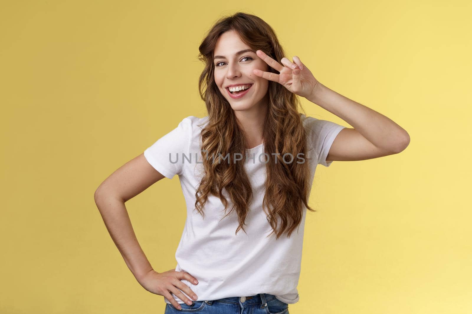 Girl having fun feel happy enthusiastic enjoy perfect summer day share positivity upbeat mood show peace victory sign near cheek tilt head smiling silly carefree stand yellow background. Lifestyle.