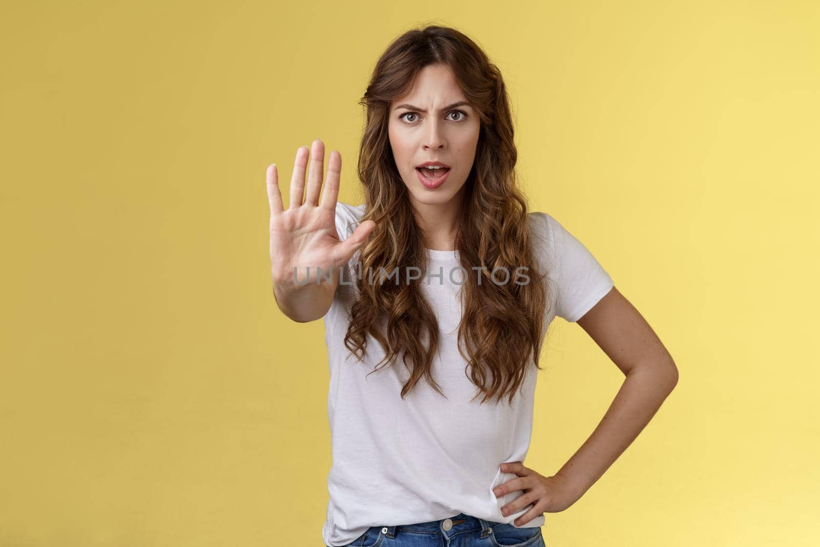Stop right there fashion police. Serious-looking confident young curly-haired girl pull hand enough prohibition gesture demand end situation forbid friend drive stand yellow background.