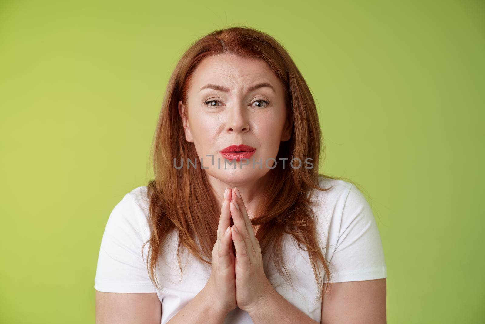 Please need help asap. Tender timid redhead middle-aged woman plead press palms together pray begging hopeful sincere look camera, implore friend favour stand green background silly by Benzoix