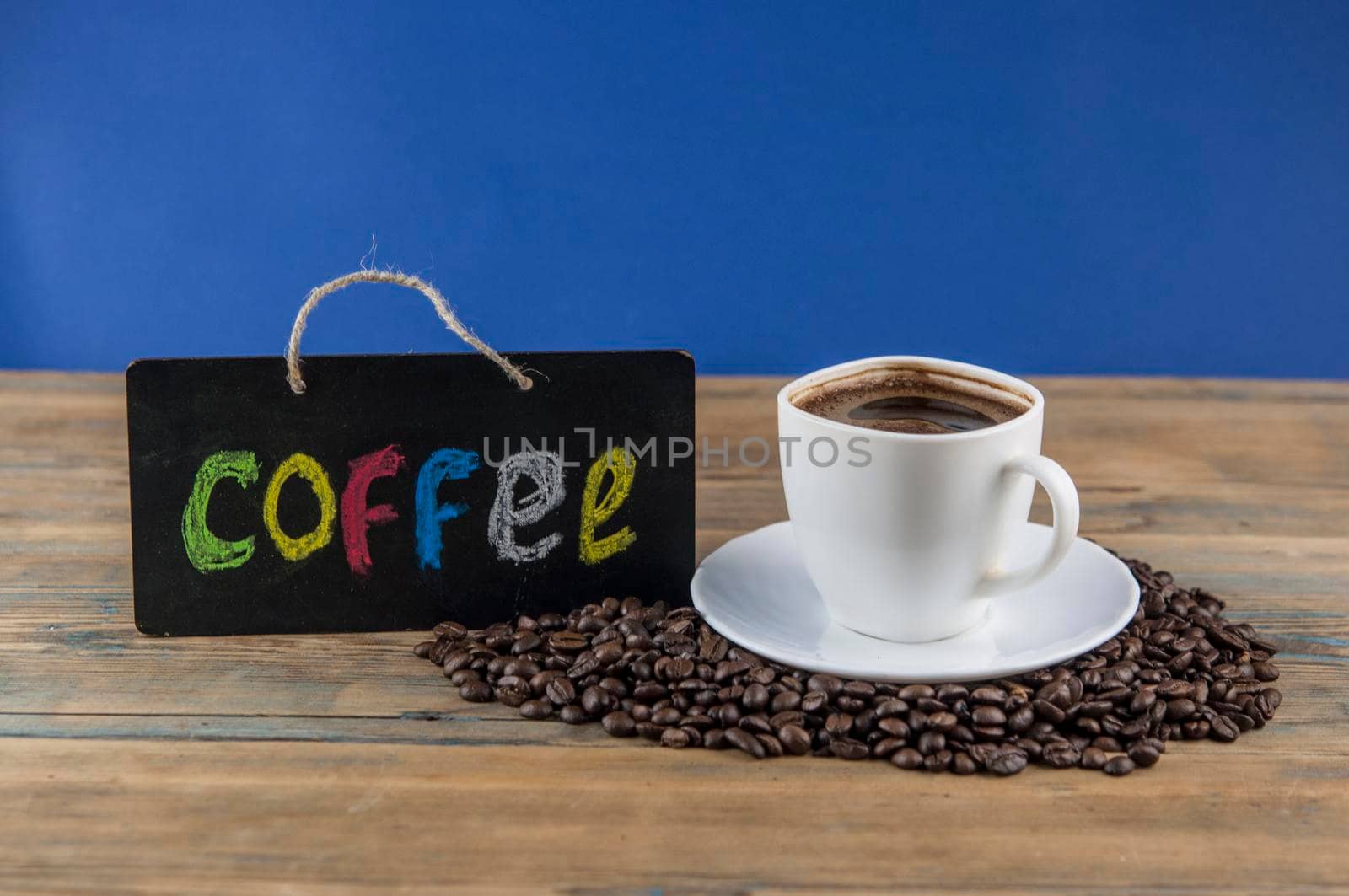White ceramic cup of coffee and blackboard with inscription "coffee" writen colorful alphabet. Coffee break, morning awakening concept.