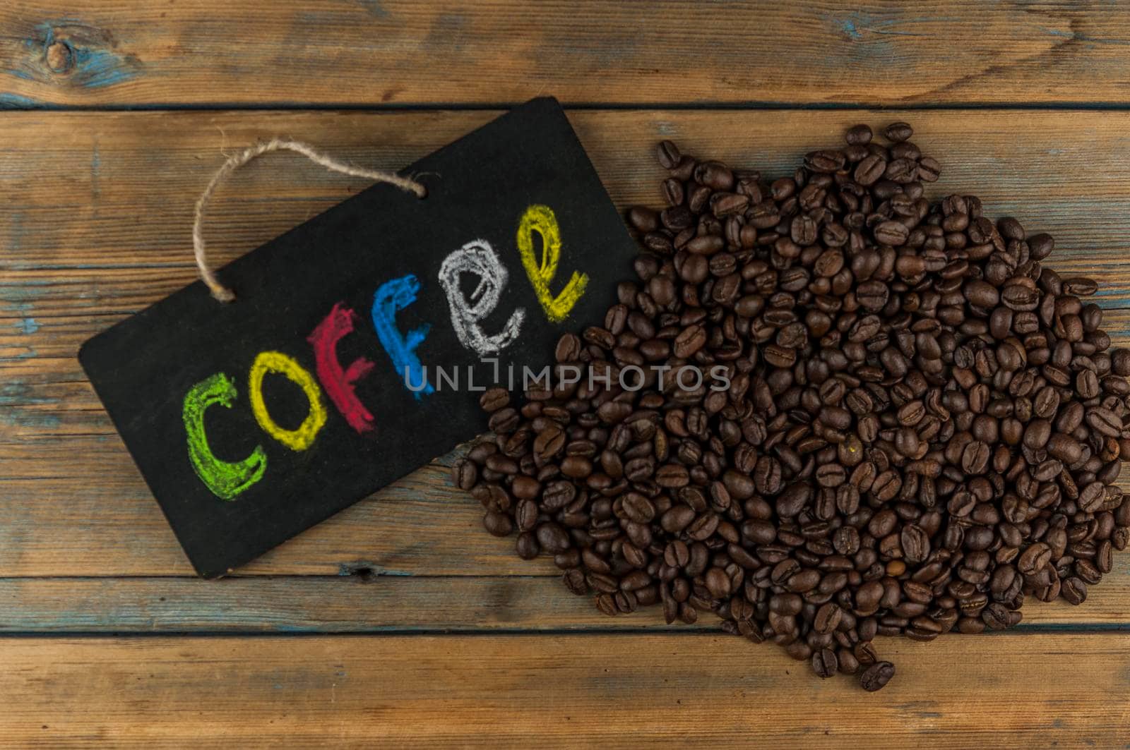 Heap coffee beans and a board with the inscription "coffee" written in a colorful alphabet. Coffee break, the concept of waking up in the morning. Top view