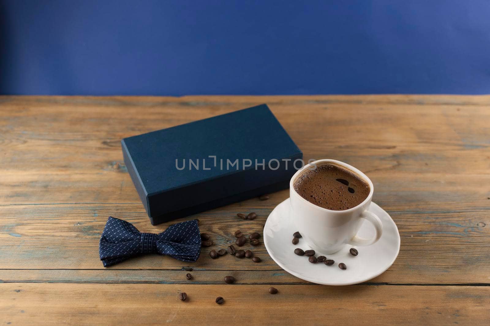 White ceramic cup of coffee with bow tie and gift box on old wooden table with some beans. Father day card.