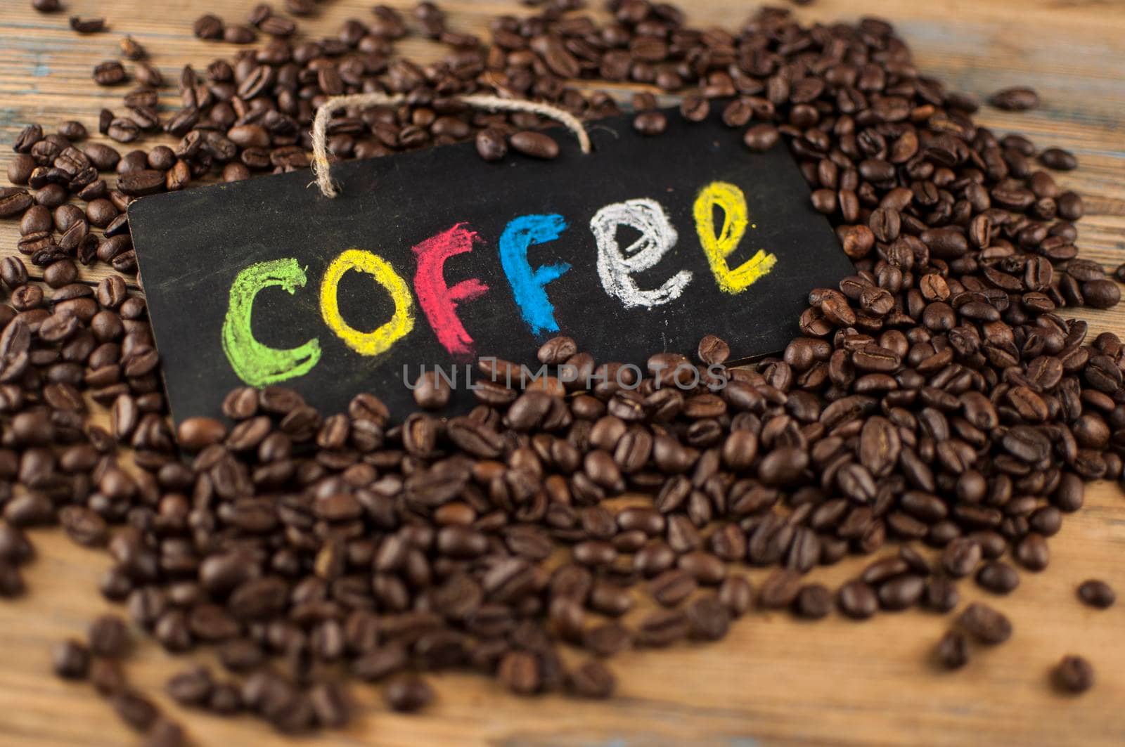 Heap coffee beans and a board with the inscription "coffee" written in a colorful alphabet. Coffee break, the concept of waking up in the morning. Top view