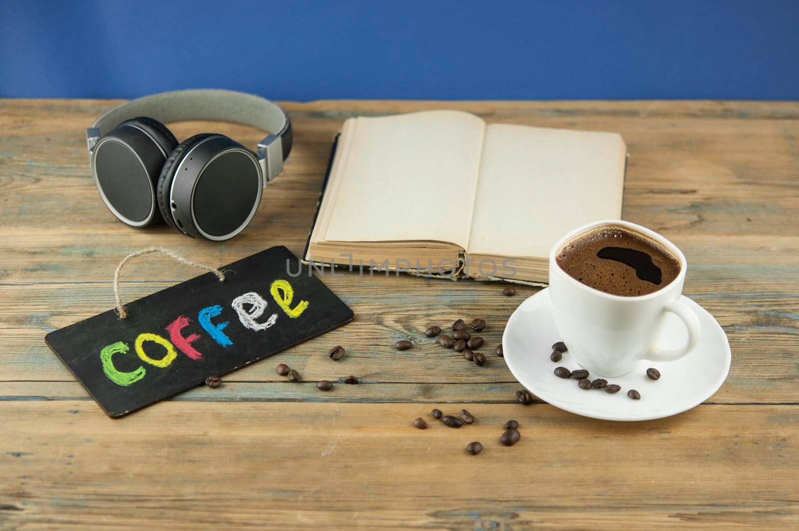 A cup of coffee, headphone, open book and a board with the inscription "coffee" written in a colorful alphabet. Coffee break, the concept of waking up in the morning.
