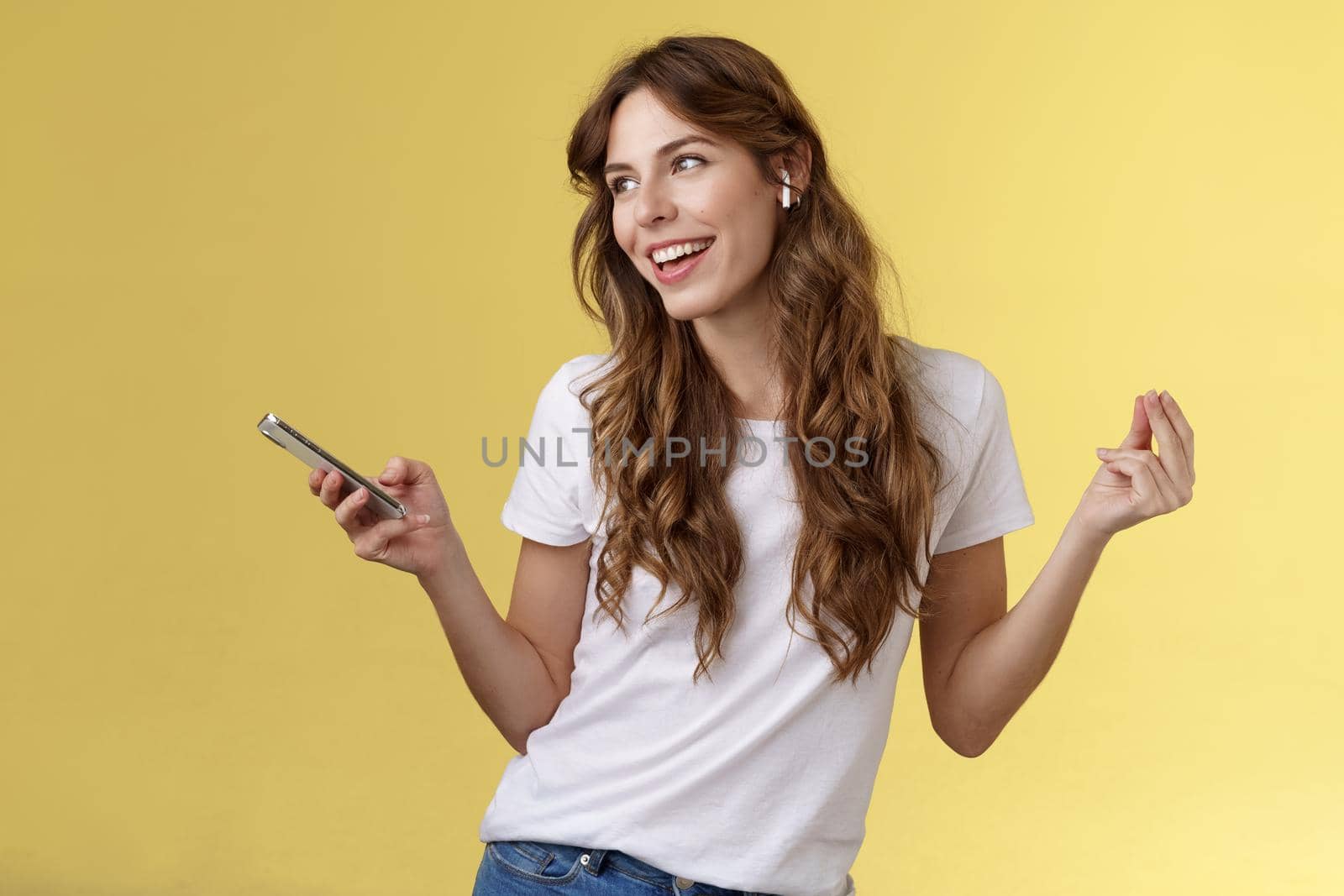 Girl enjoying music listening song wireless earbuds dancing lively carefree look away smiling broadly hold smartphone found new track partying alone soundtrack favorite movie yellow background by Benzoix