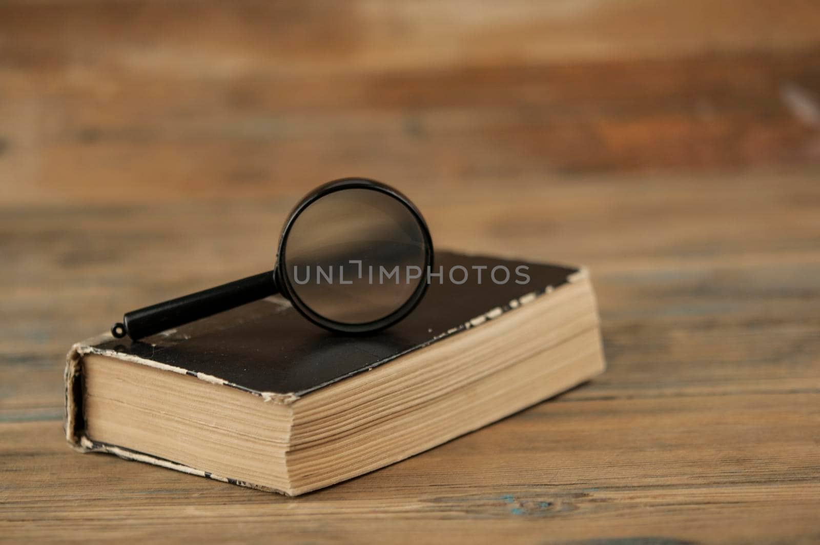 Magnifying glass with close old book on wood table  by inxti
