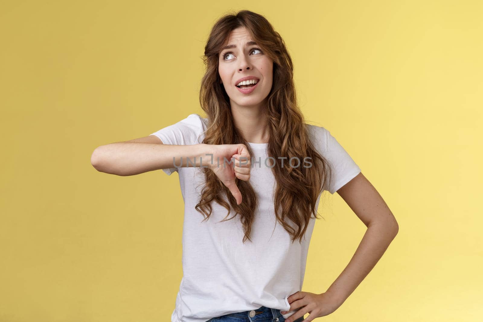 Blah blah boring. Unimpressed apathetic snobbish attractive curly-haired girl look away express scorn disdain show thumb down frowning sharing negative judgement bad opinion yellow background.