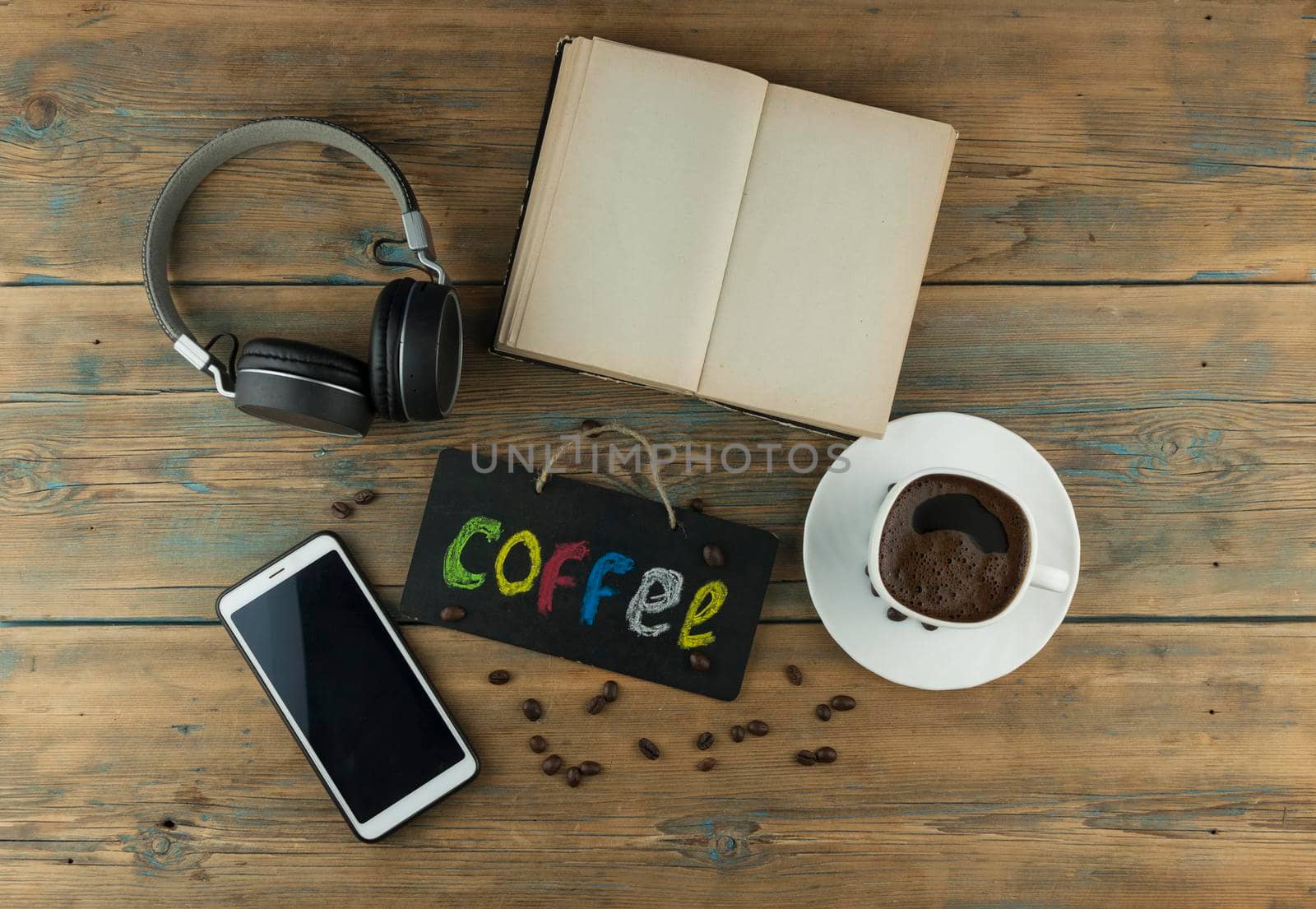 A cup of coffee, headphone, open book and a board with the inscription "coffee" written in a colorful alphabet. Coffee break, the concept of waking up in the morning. Top view