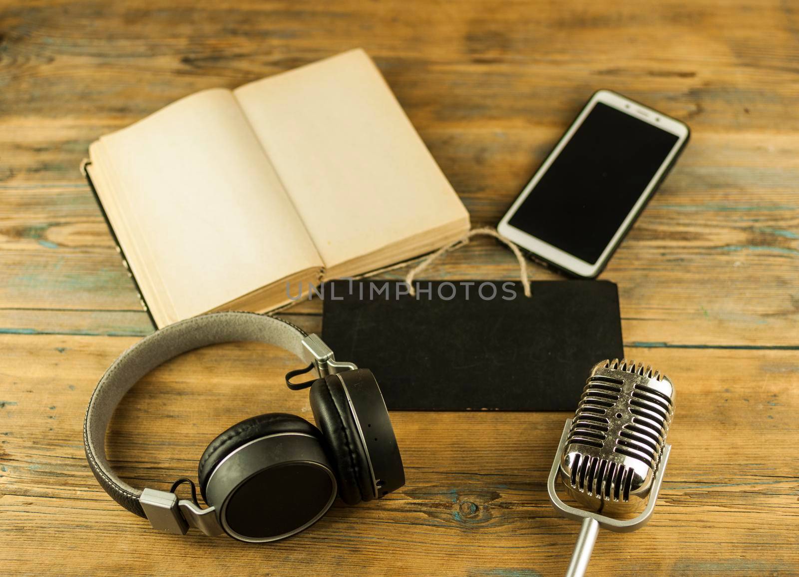 Black headphones with smarphone and open book are on the wooden table. Audio book concept. Distance learning by inxti