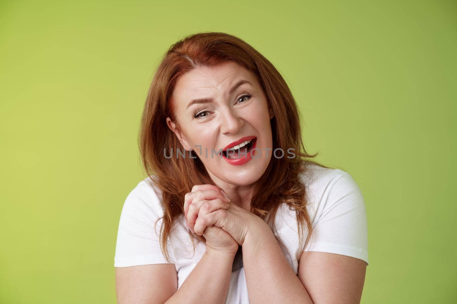 Close-yp touched tender kind redhead middle-aged granny. sighing look admiration delight clasp hands heartwarming lovely scene smiling tilting head impressed satisfied stand green background.