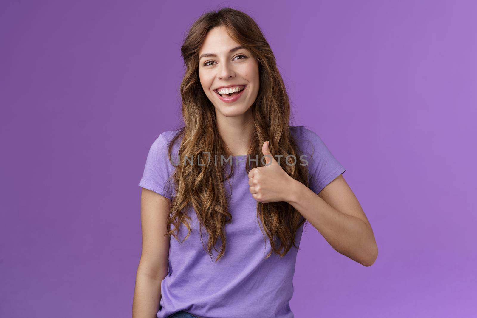 Cheerful supportive lively outgoing caucasian girl like your idea positive opinion give approval show thumbs up satisfied smiling broadly accepting great plan stand purple background.