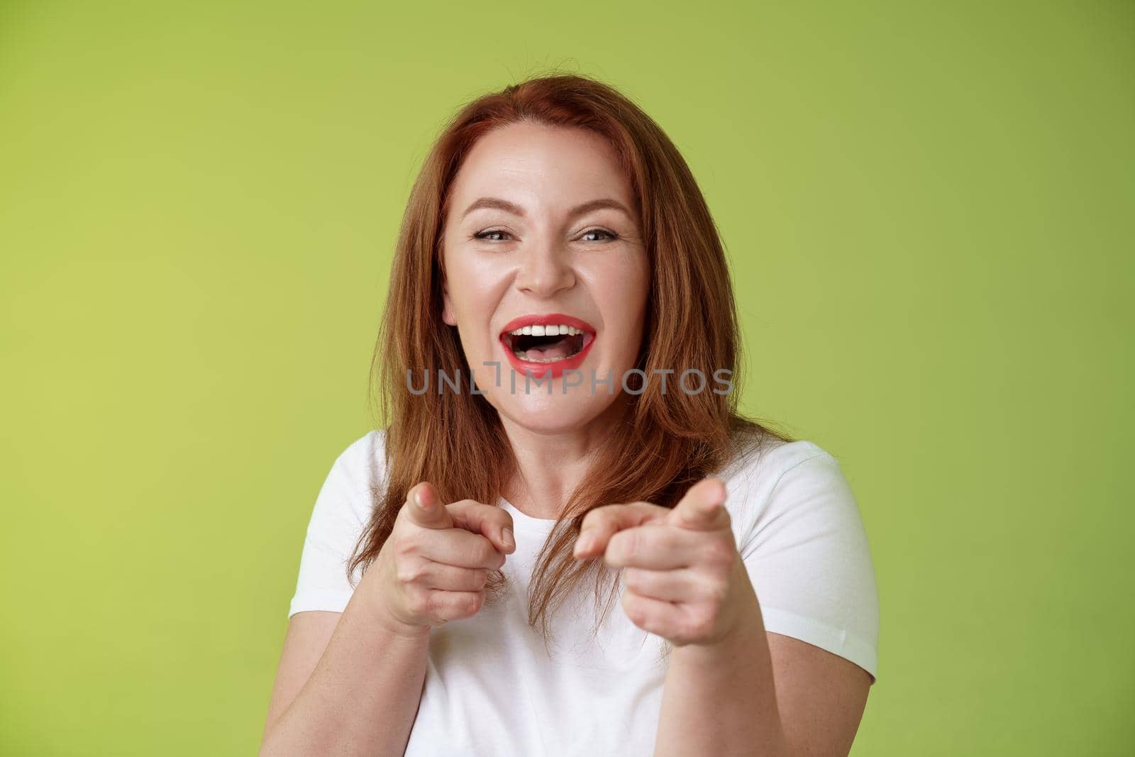 You did best. Friendly joyful enthusiastic redhead ginger middle-aged female pointing index fingers camera finger pistol gesture smiling broadly congratulate cheer coworker stand green background.