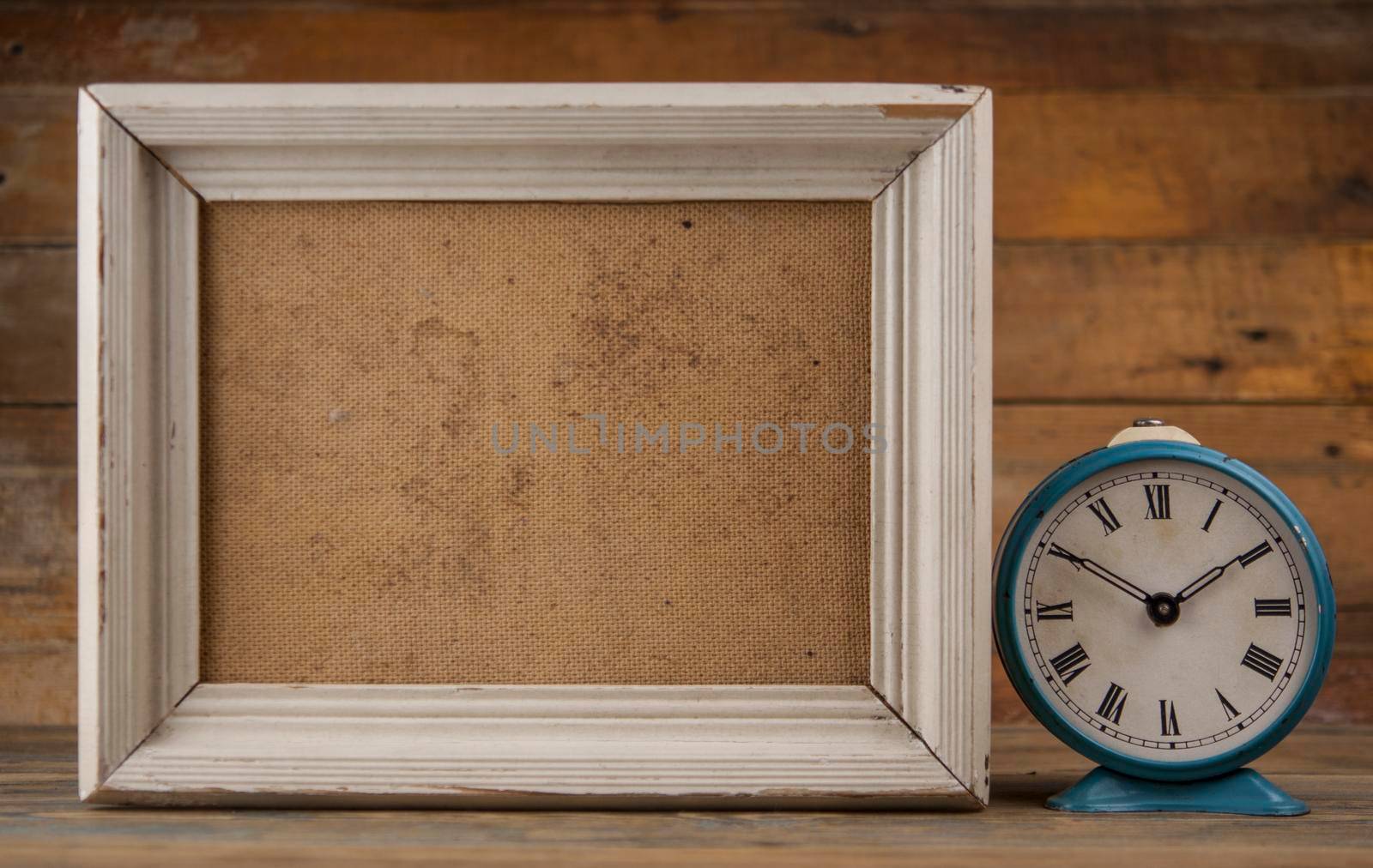 Blank old wooden frame with alarm clock on parquet floor