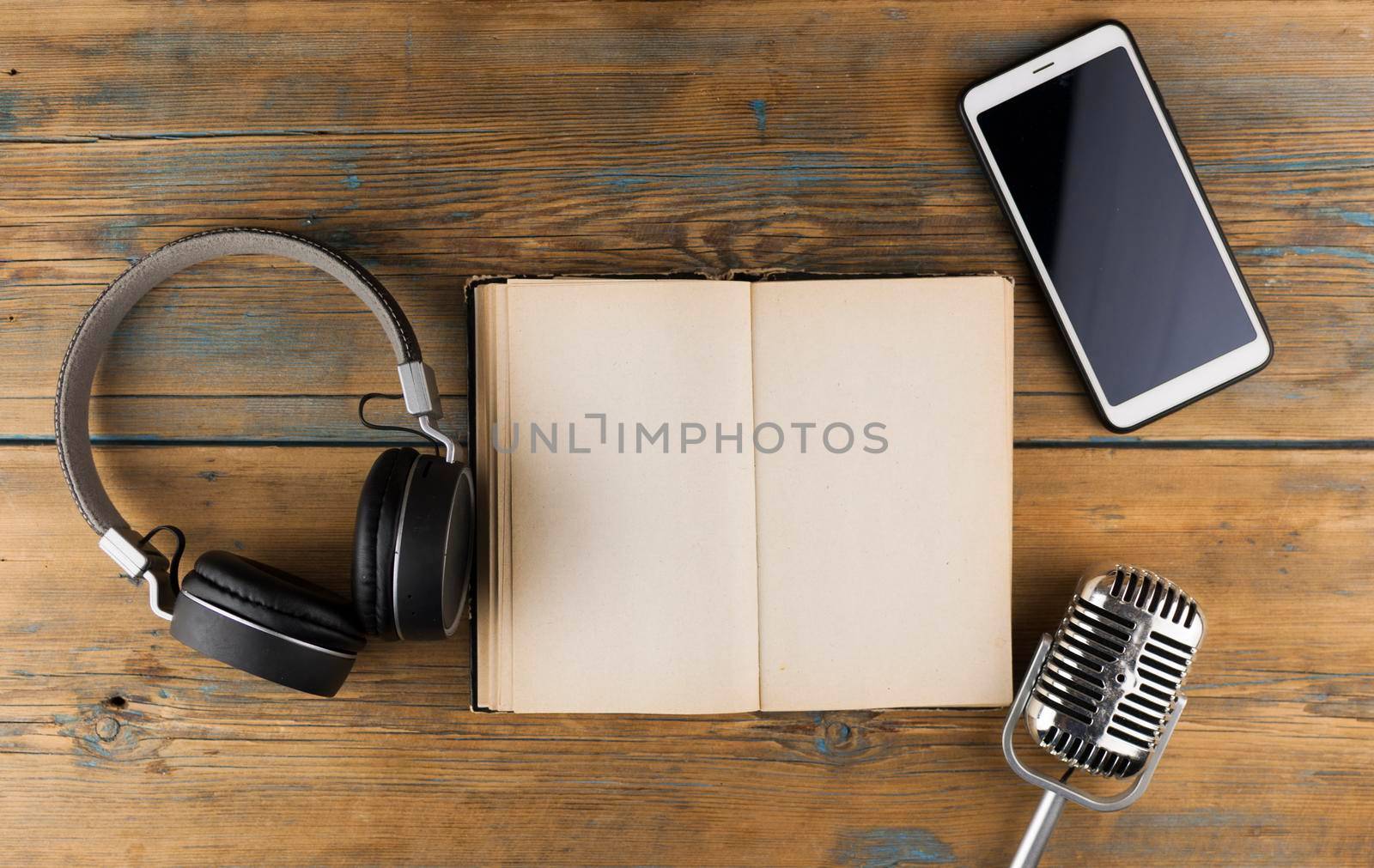 Black headphones with smarphone and open book are on the wooden table. Audio book concept. Distance learning. Close up, copy space, background.